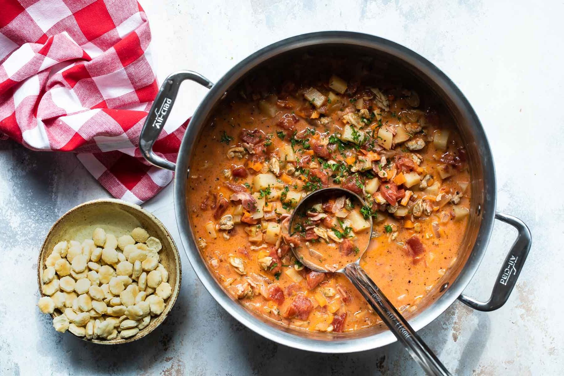 A pot of Manhattan clam chowder soup with a ladle resting in it.