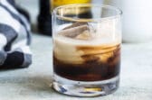 A white Russian cocktail with a bottle of Kahlua in the background.