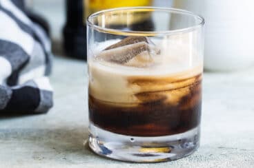 A white Russian cocktail with a bottle of Kahlua in the background.