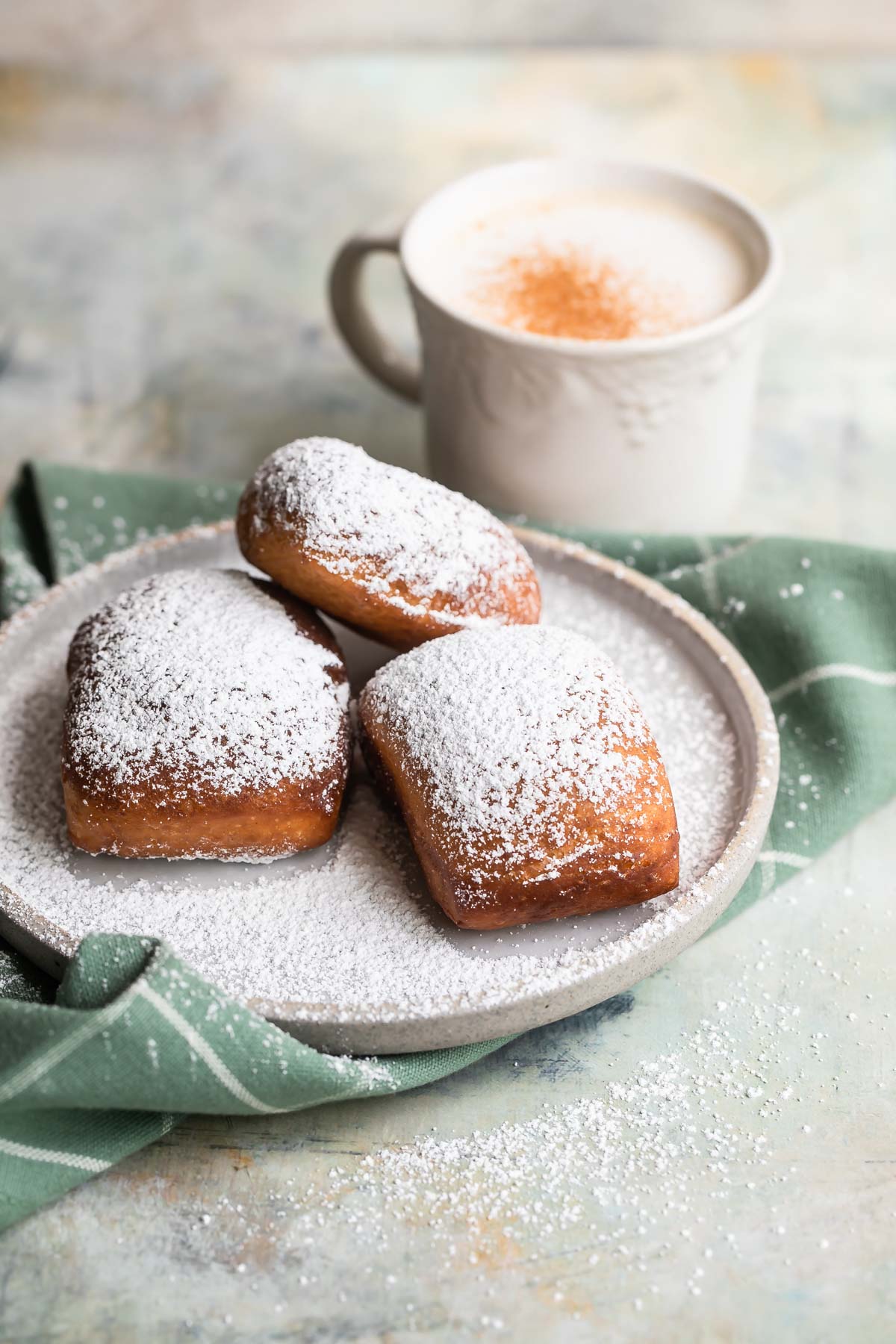 Beignets on a plate next to a coffee mug with liquid in it.