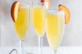 Three bellinis garnished with fresh peach slices.