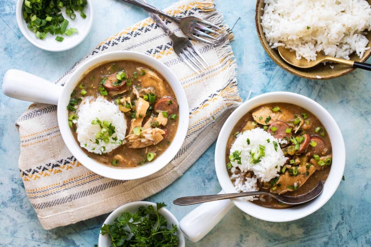 Chicken gumbo in two small white bowls with rice on top.