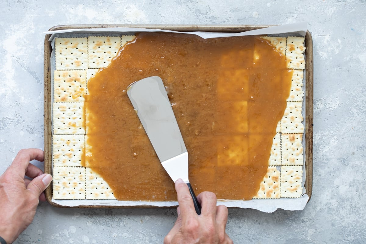 Someone spreading the sugar and butter mixture over the saltine crackers.