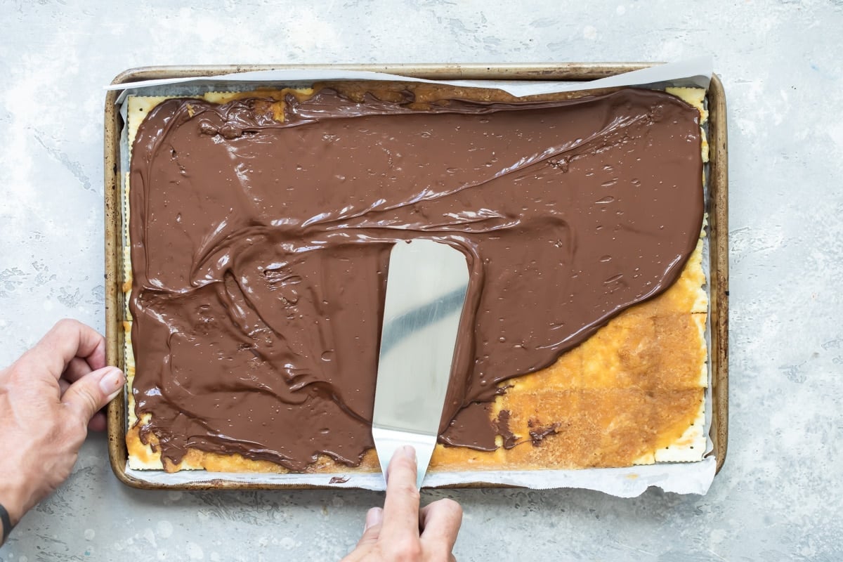 Chocolate being spread onto the layer of saltine crackers.