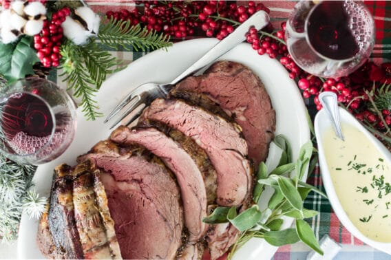 Prime rib cut into slices on a white platter with a serving fork.