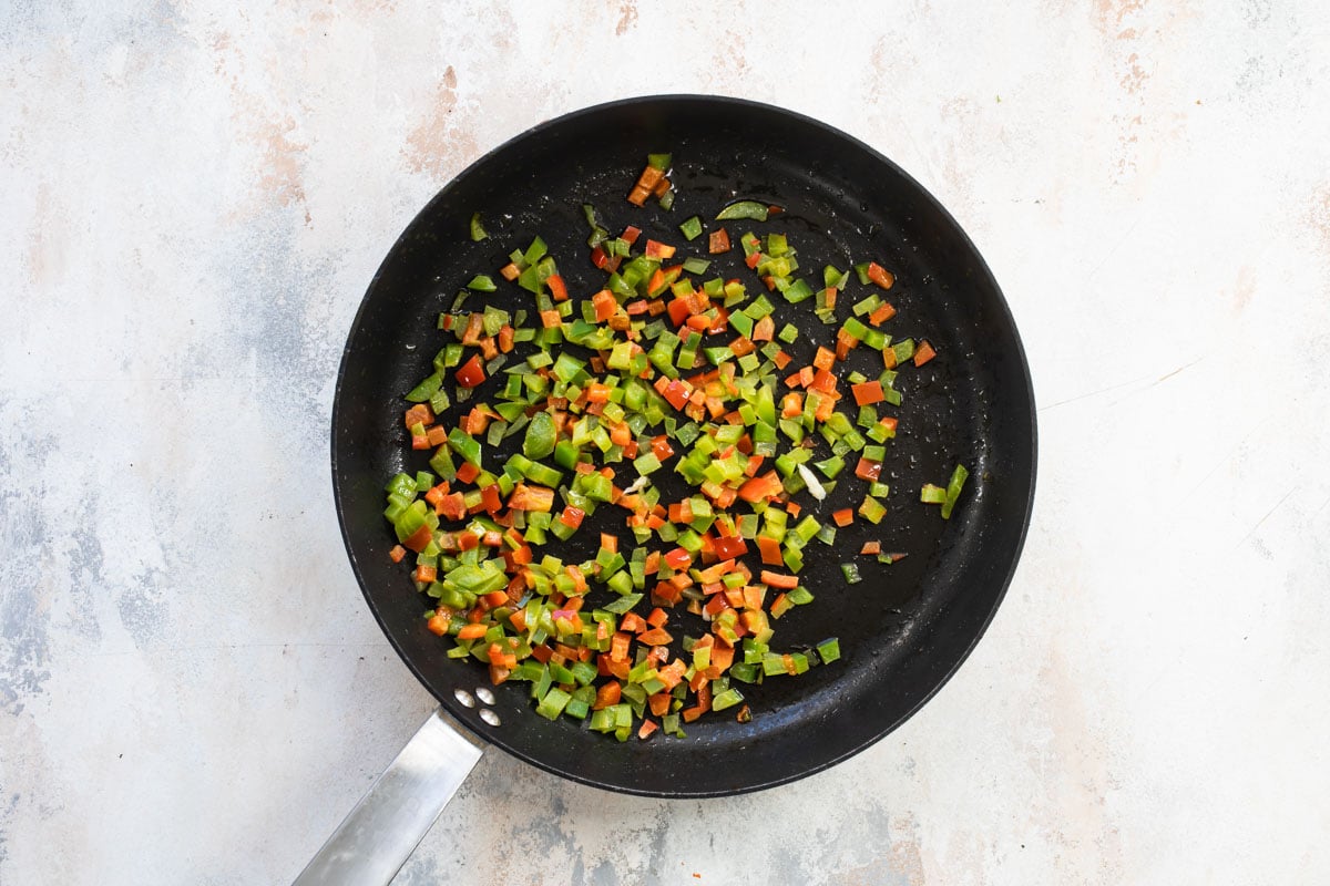 Diced vegetables getting cooked in a black skillet.