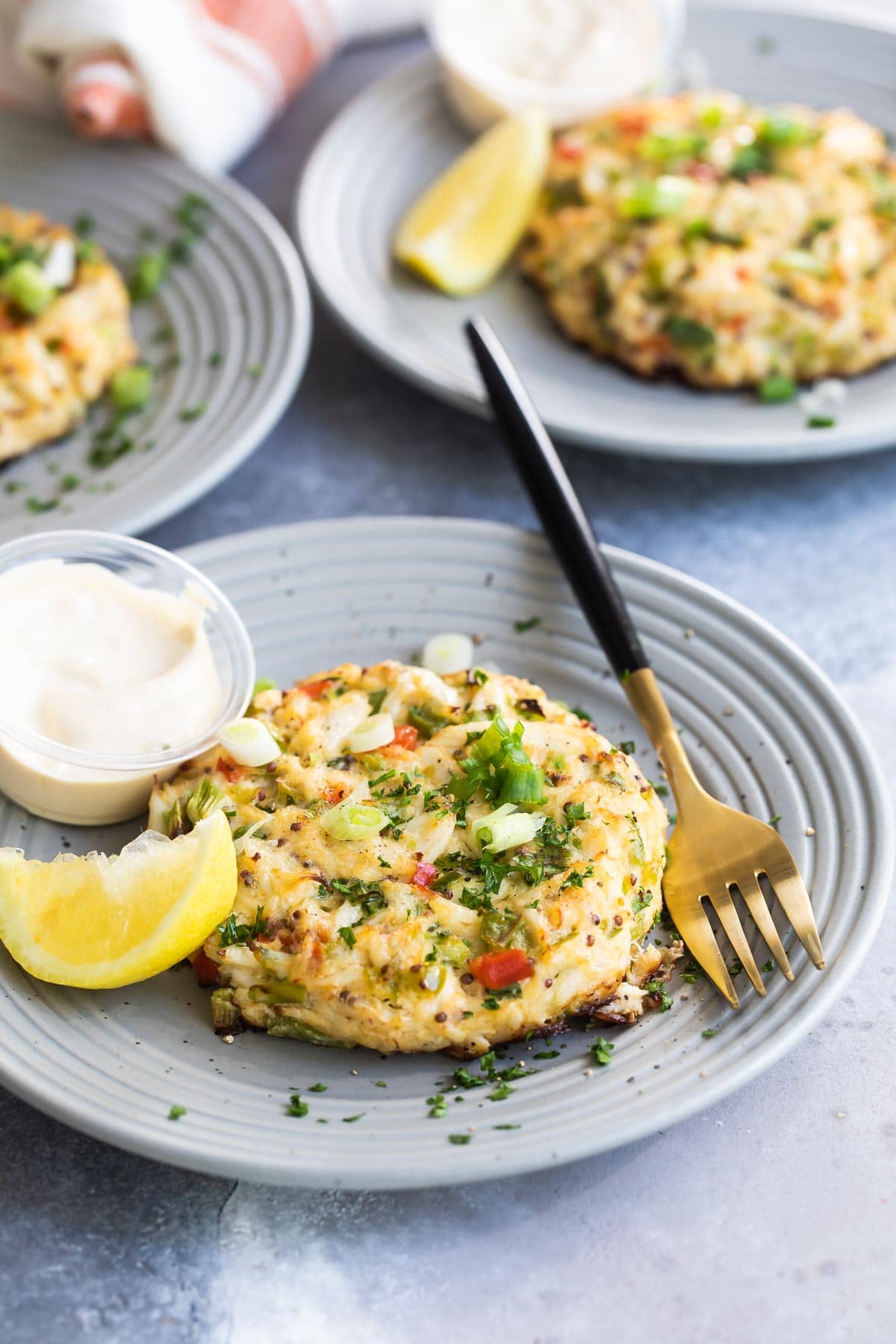 A crab cake on gray plate with a lemon wedge garnish.