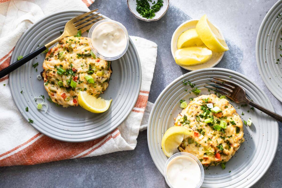 A crab cake on gray plate with a lemon wedge garnish.