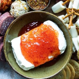 Pepper jelly poured over a block of cream cheese on a charcuterie board.