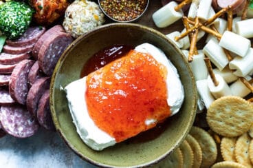 Pepper jelly poured over a block of cream cheese on a charcuterie board.