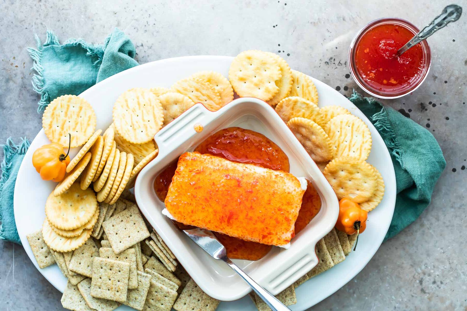Pepper jelly poured over a block of cream cheese on a charcuterie board.