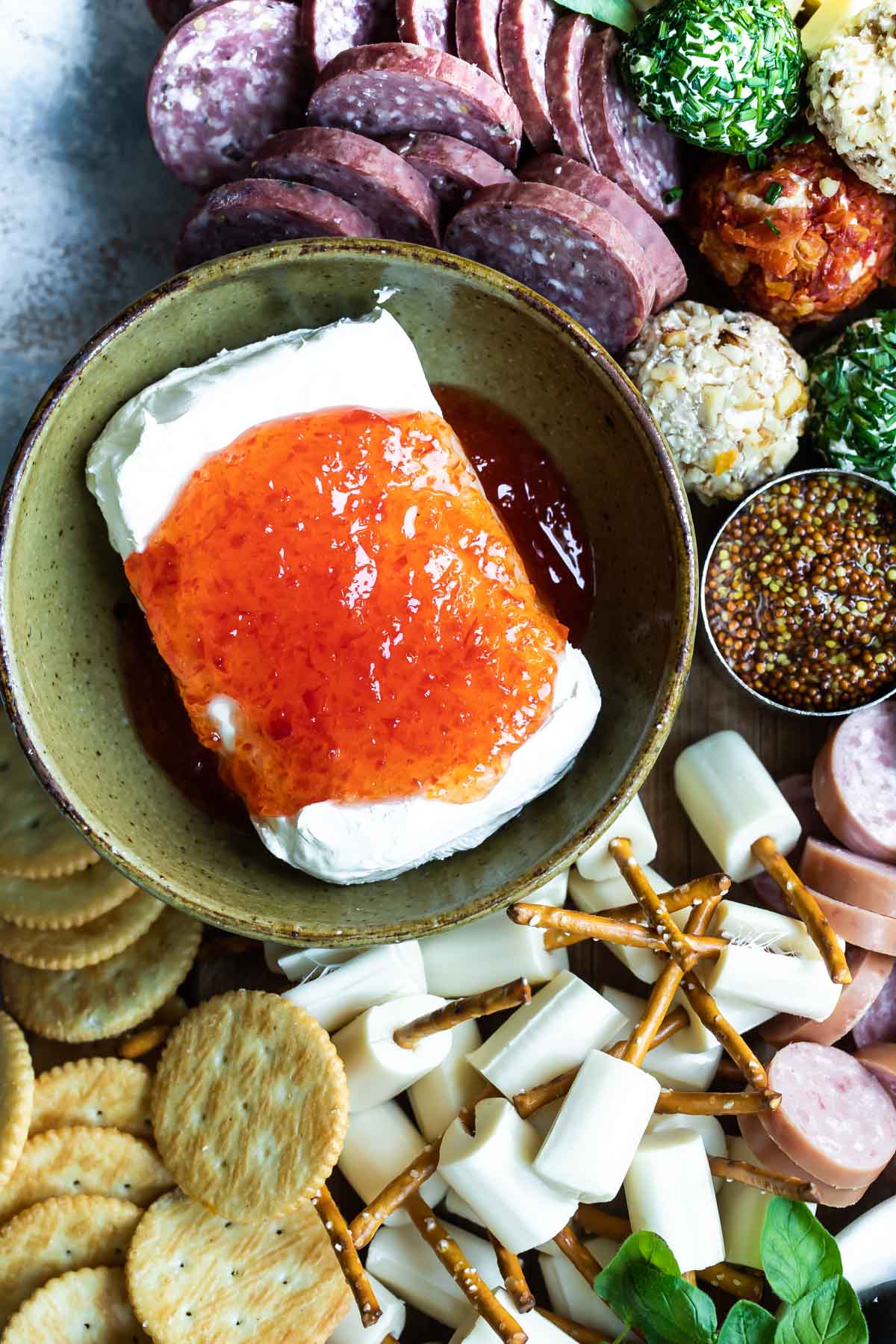 Pepper jelly poured over a block of cream cheese on a charcuterie board.