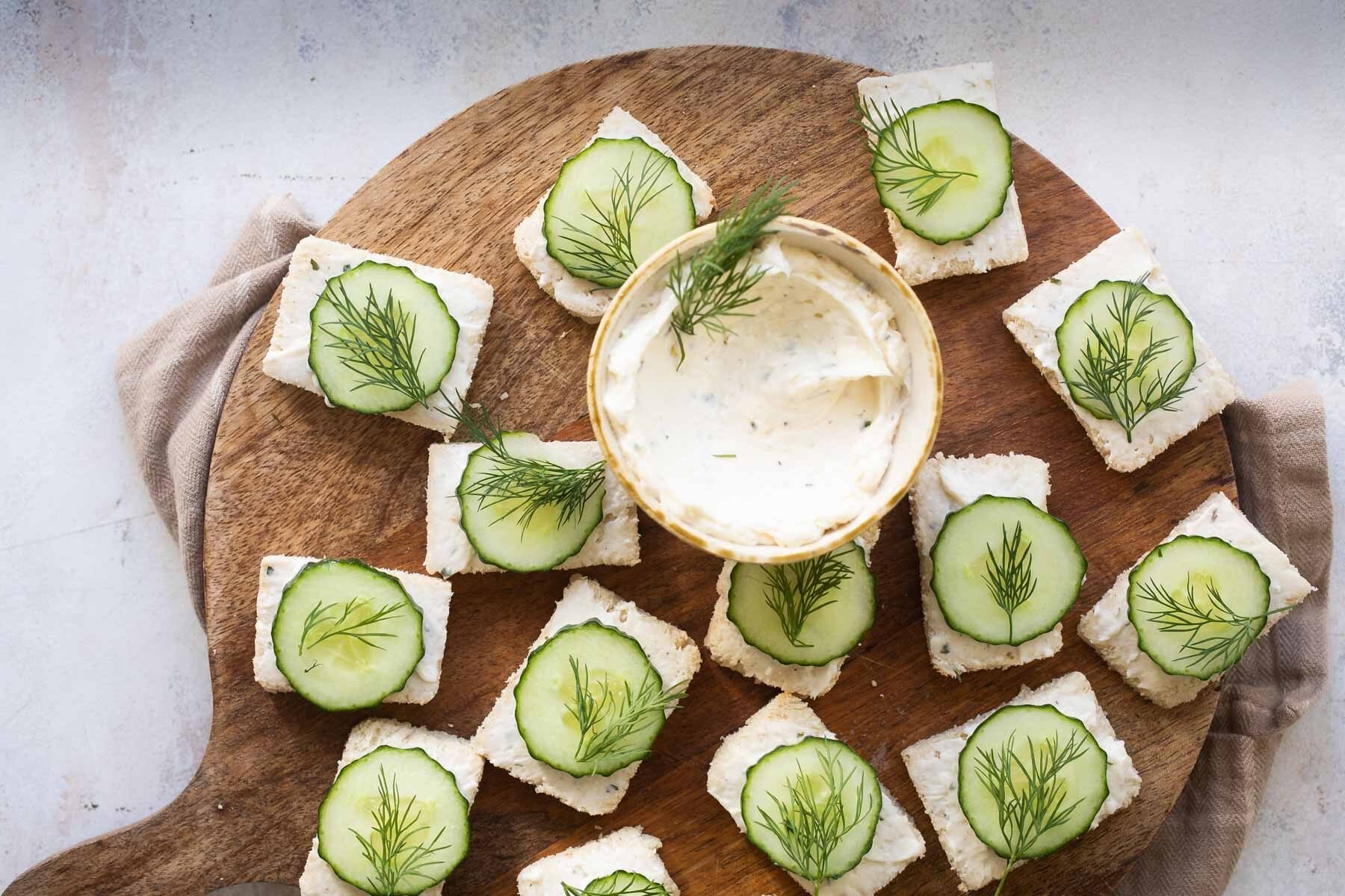 Cucumber sandwiches on a round wooden platter.