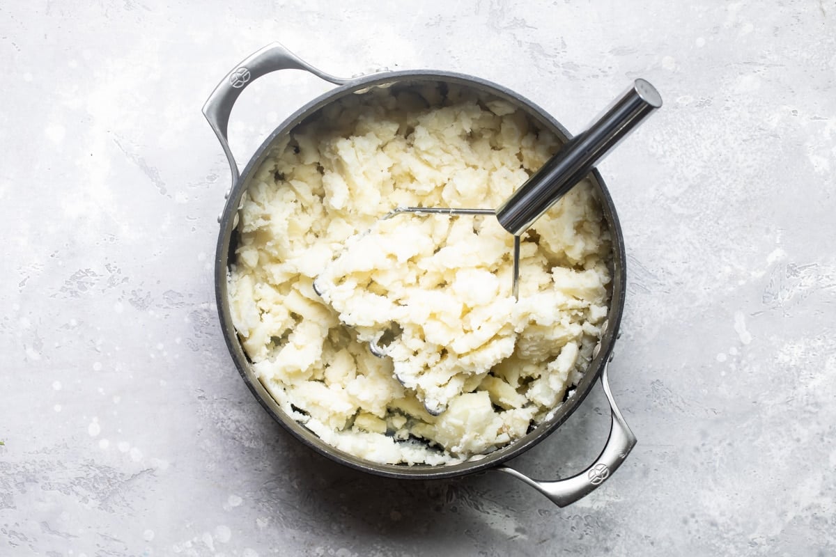 Mashing boiled potatoes in a pot.