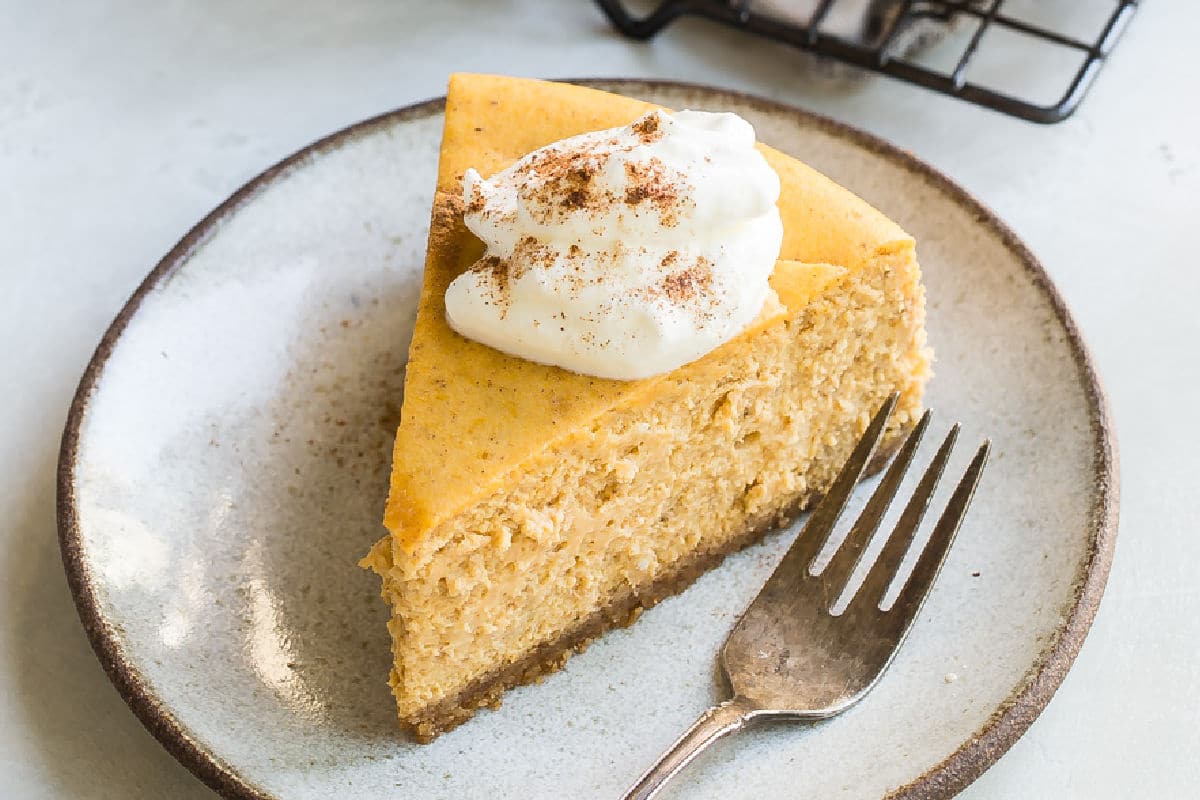 A slice of pumpkin cheesecake with whipped cream on a plate.