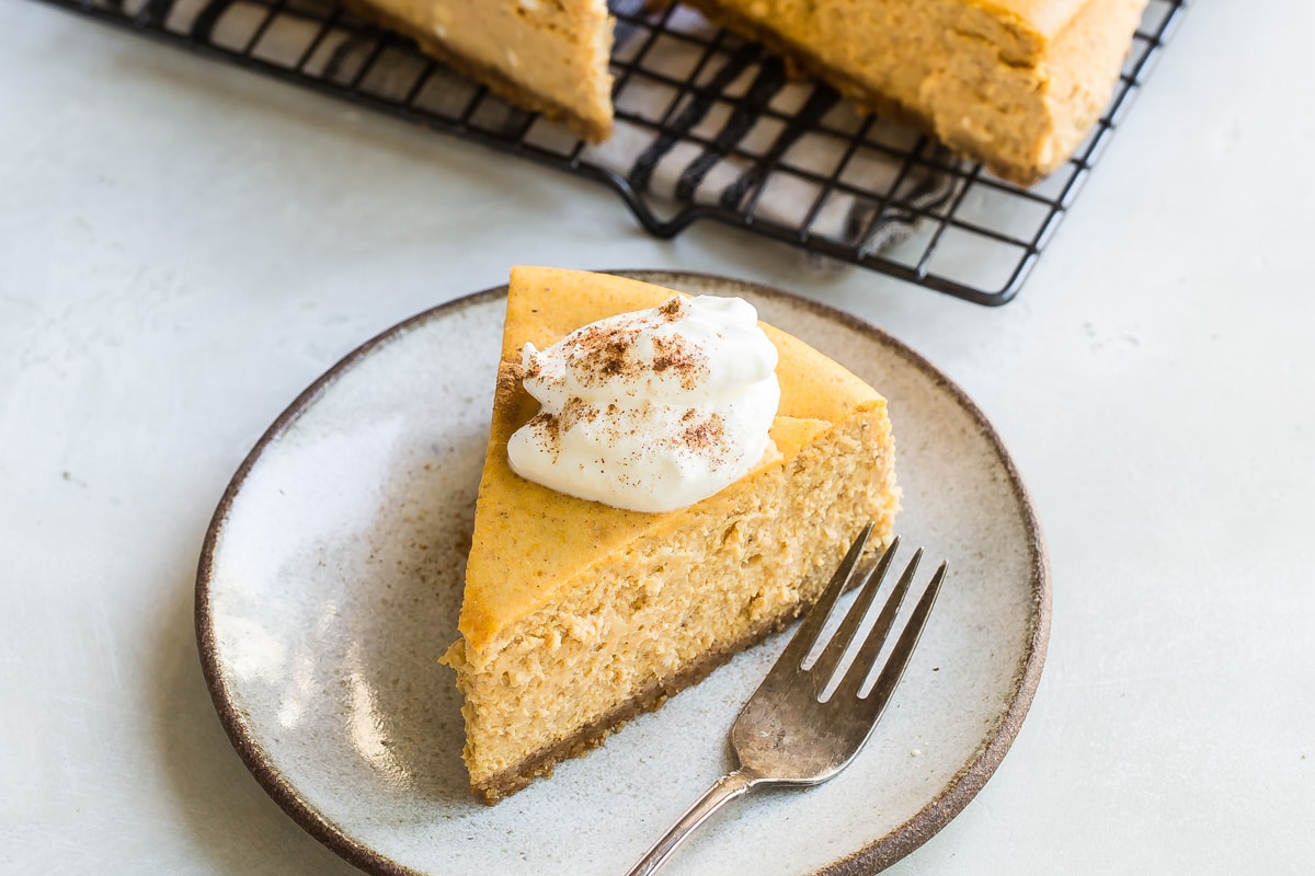 A slice of pumpkin cheesecake with whipped cream on a plate.