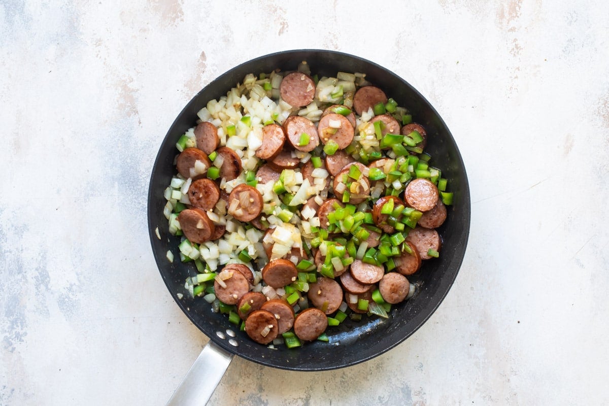 Andouille sausages with onion and peppers being cooked in a frying pan.