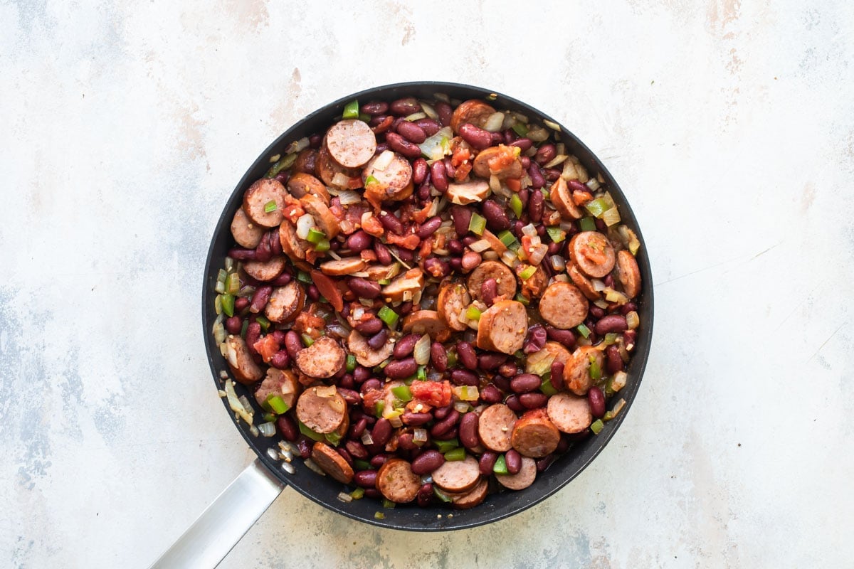 Andouille sausages, beans, onion and peppers being cooked in a frying pan.