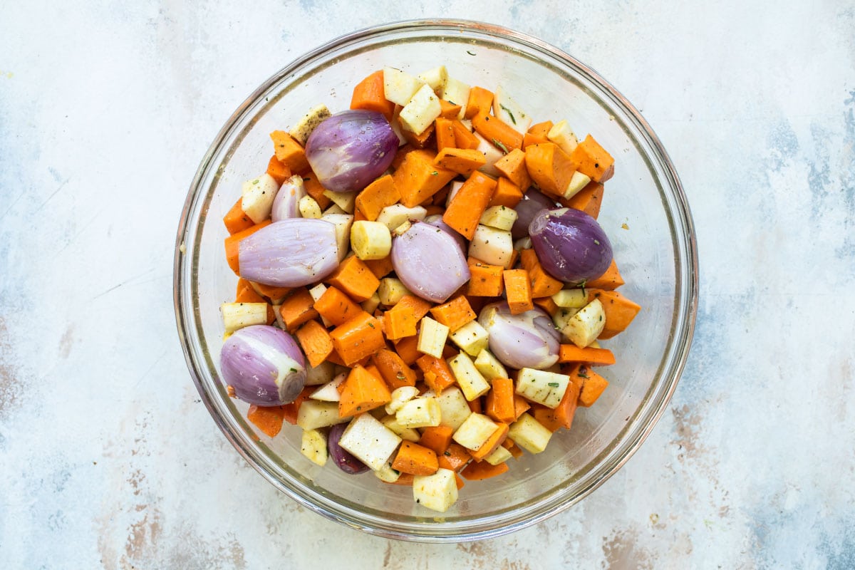 Roasted root vegetables in a clear bowl before being roasted.
