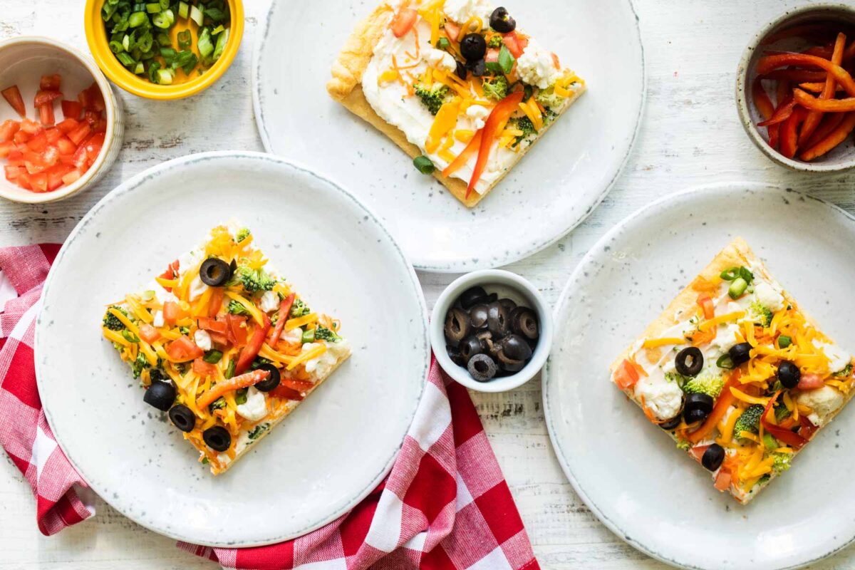 Three squares of veggie pizza on three gray plates.
