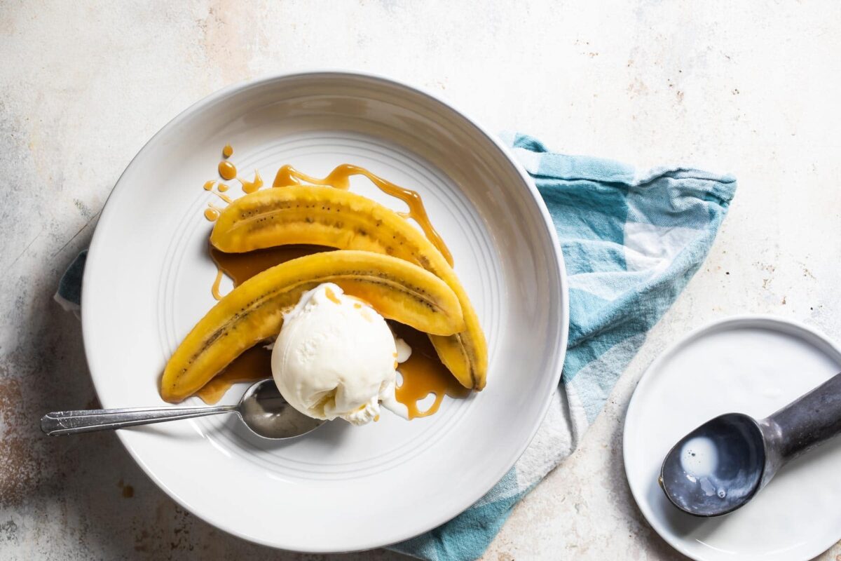 Bananas foster on white plate with a spoon resting next to it.