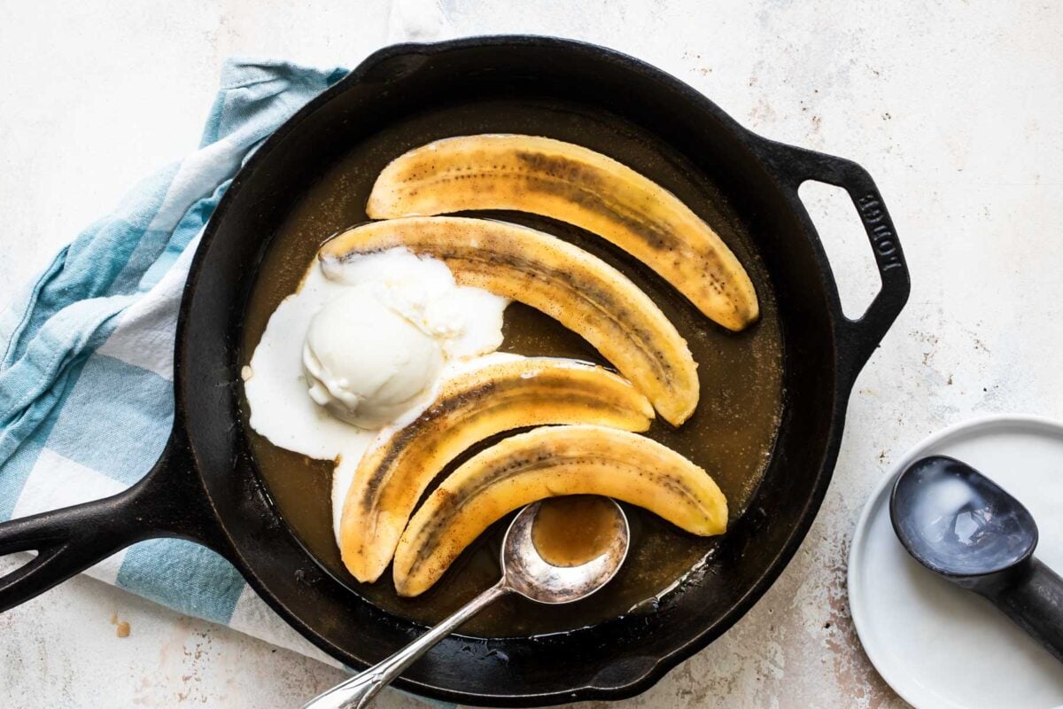 Bananas foster in a black skillet with a serving spoon resting in it.
