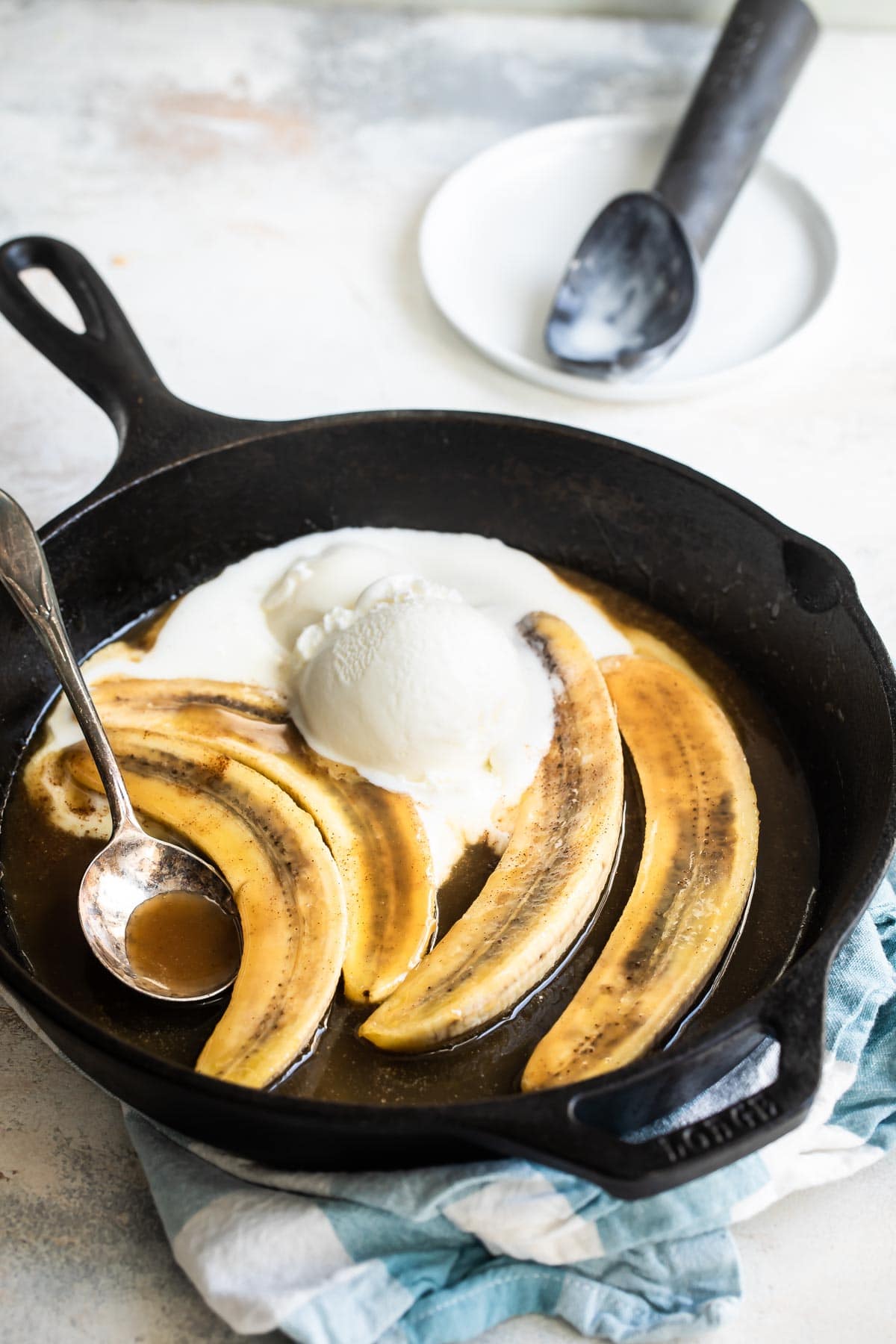 Bananas foster in a black skillet with a serving spoon resting in it.