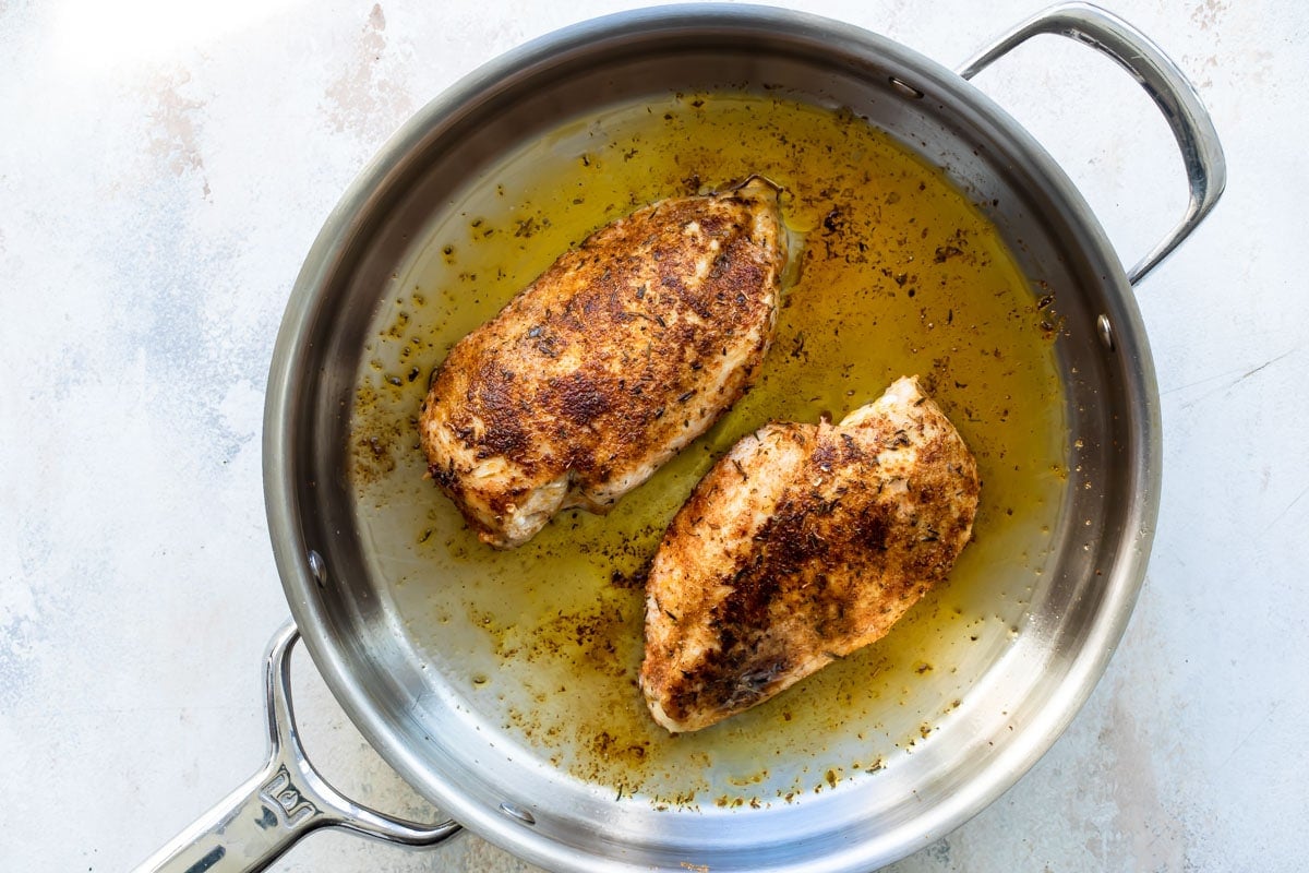 Chicken being cooked in a stainless steel skillet.