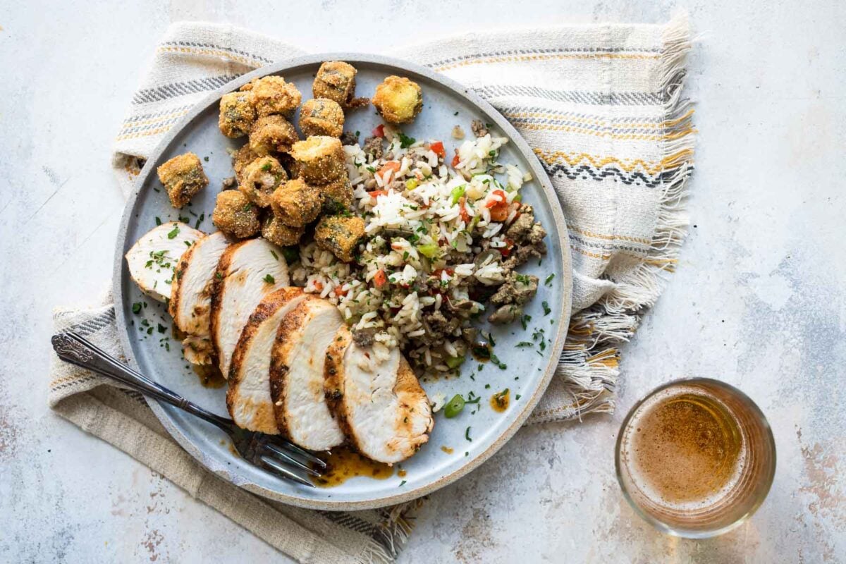Blackened chicken, dirty rice and hush puppies on a gray plate.