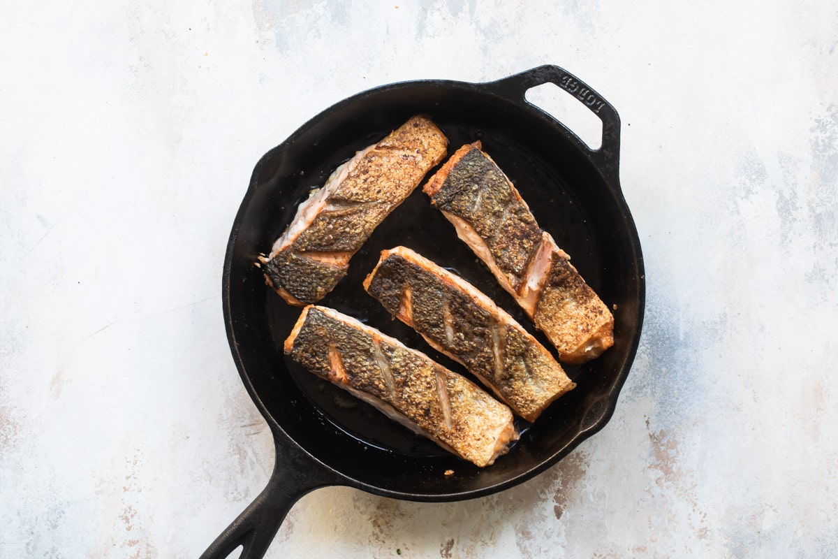 Salmon being cooked in a cast iron skillet.