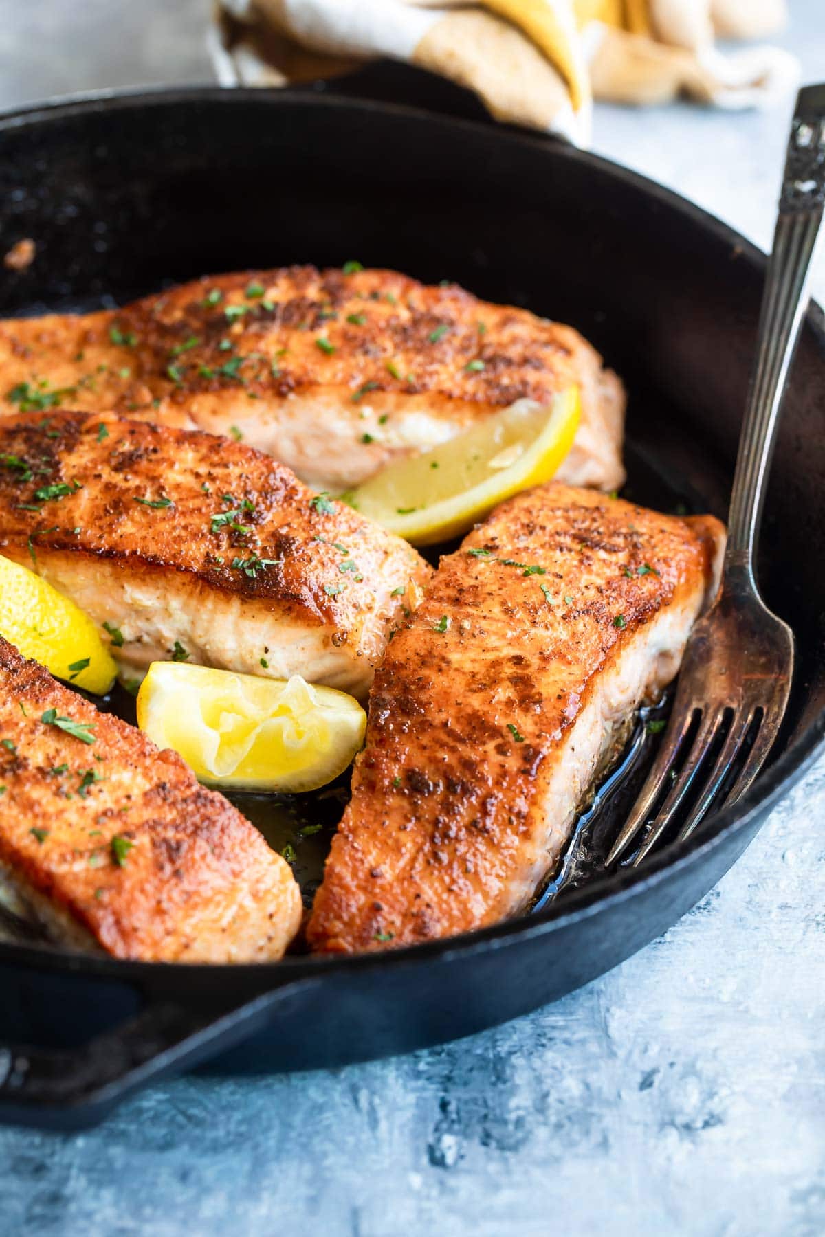 Salmon in a cast iron skillet with lemons for garnish.