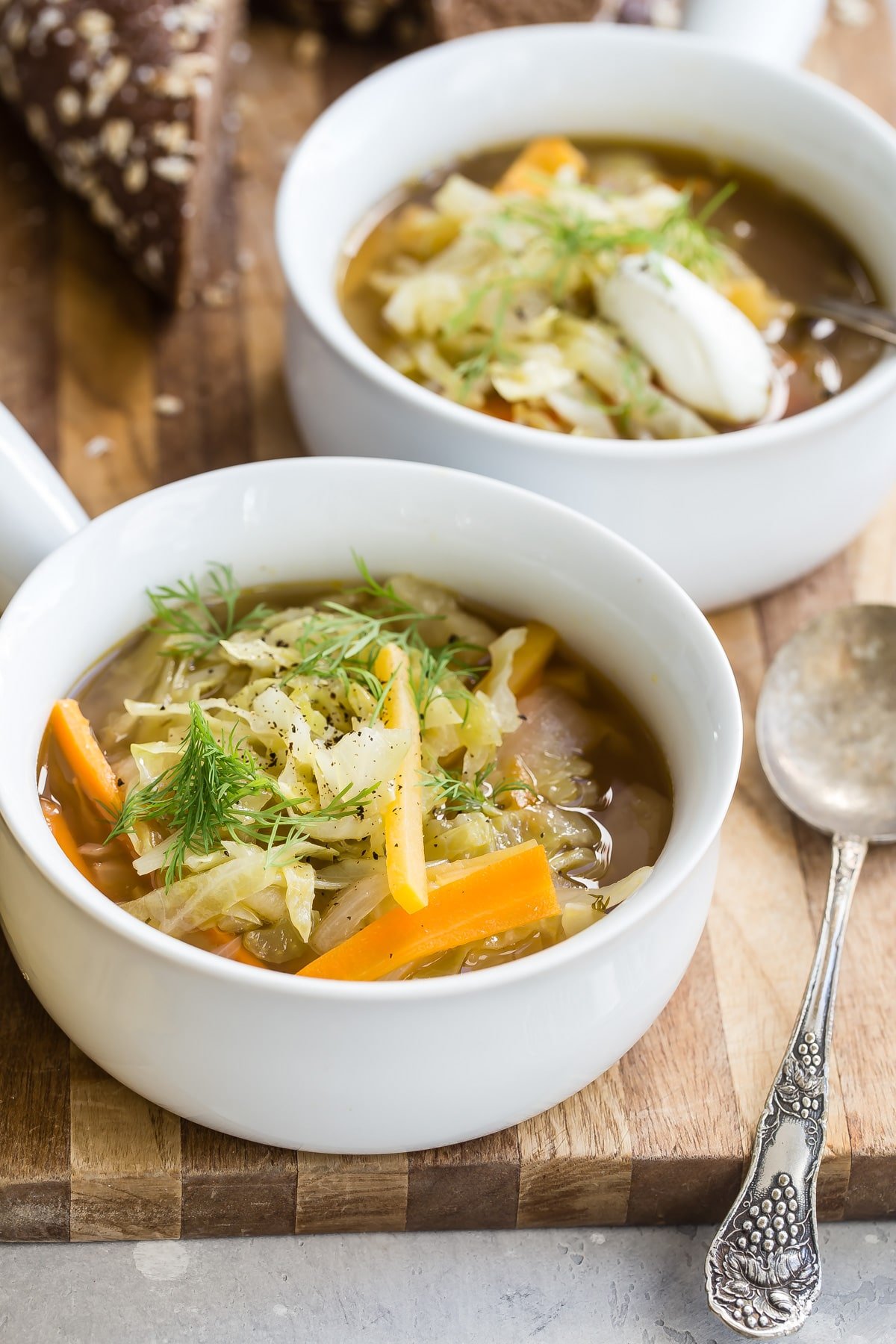 Cabbage soup in a white bowl with a silver spoon next to it.