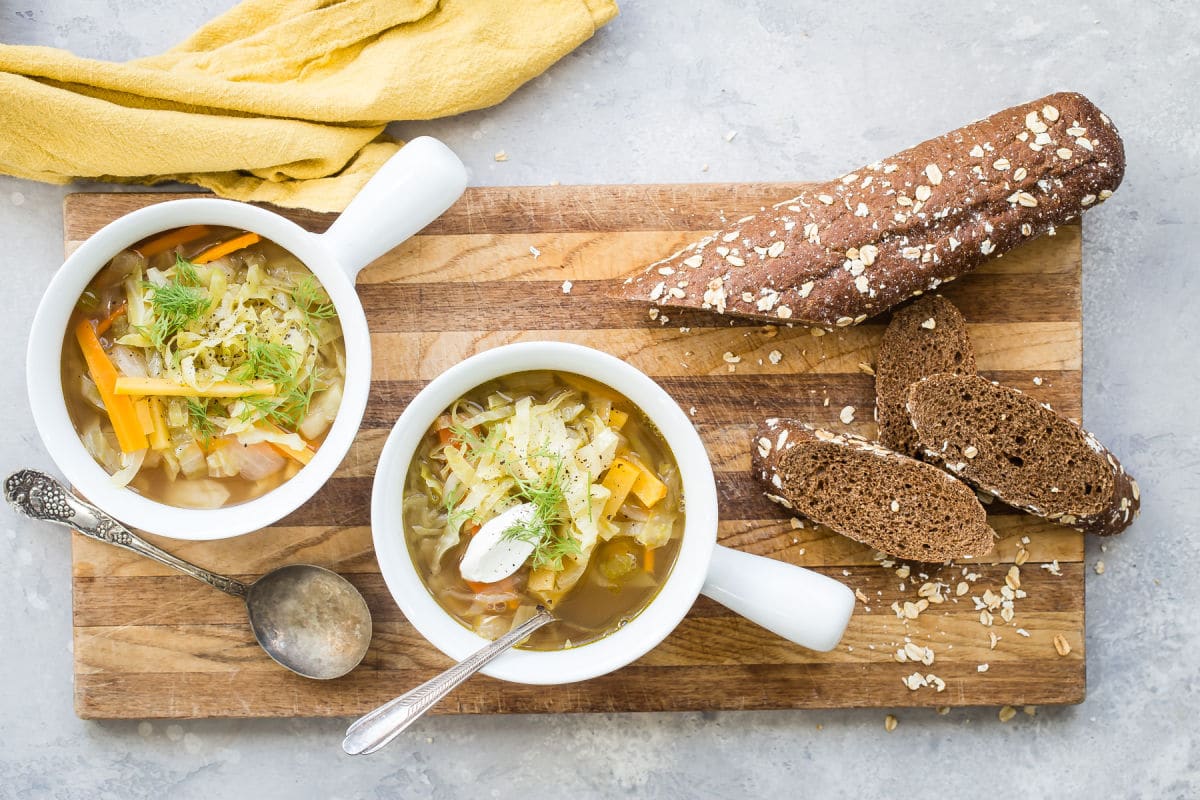 Cabbage soup in a white bowl with a silver spoon next to it.