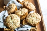 Coffee cake muffins in a basket on a wooden serving tray.