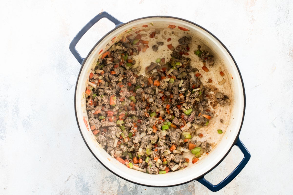 Ground pork and vegetables being cooked in a Dutch oven.