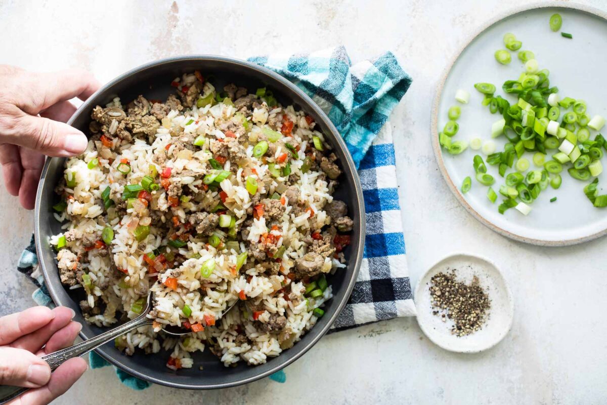 Dirty rice being scooped out of a gray serving bowl.