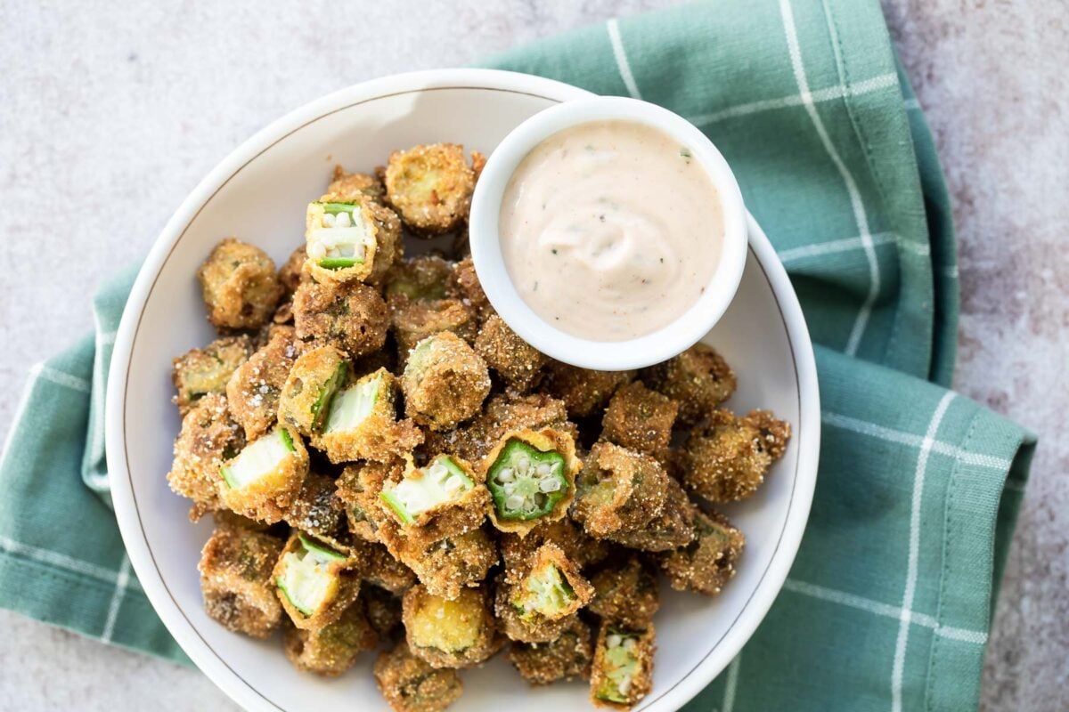 A bowl of fried okra with remoulade sauce on the side.