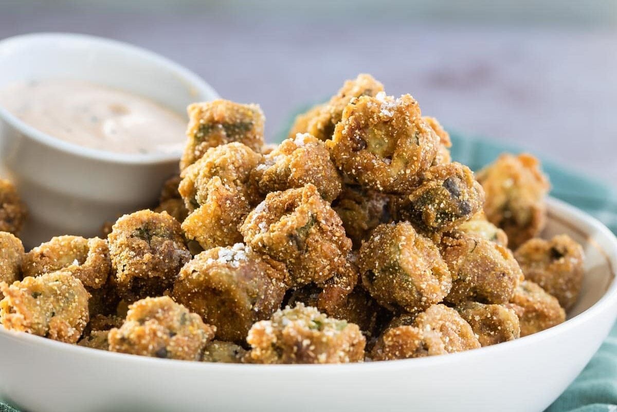 A bowl of fried okra with remoulade sauce on the side.