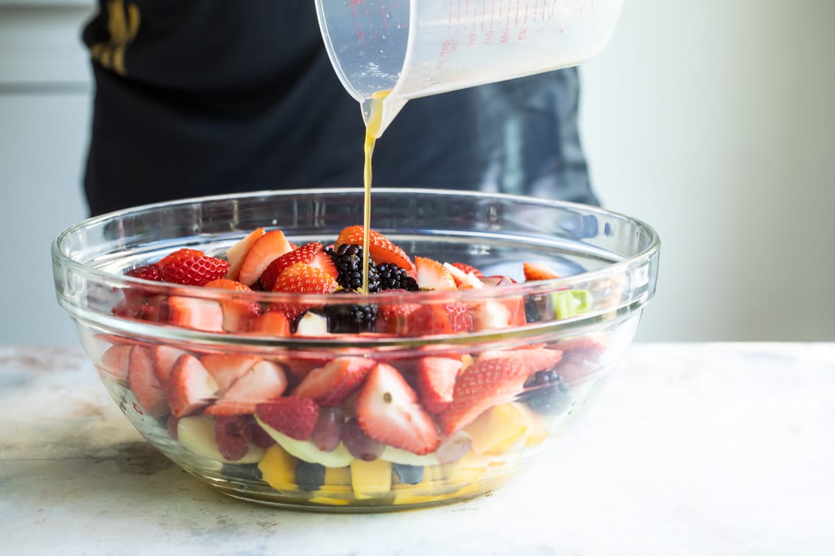 Dressing being poured into a clear bowl filled with fruit.