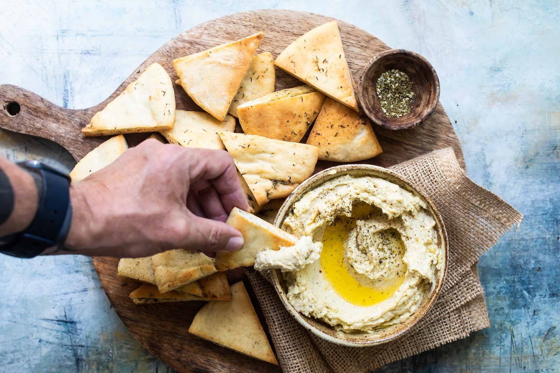 Homemade hummus with zaatar butter in a bowl with pita chips.