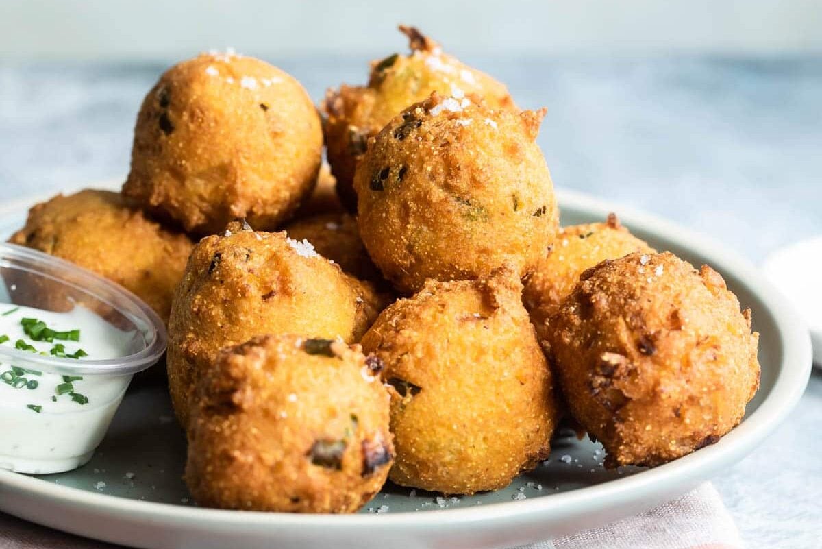 Hush puppies on a light blue plate with white dipping sauce.