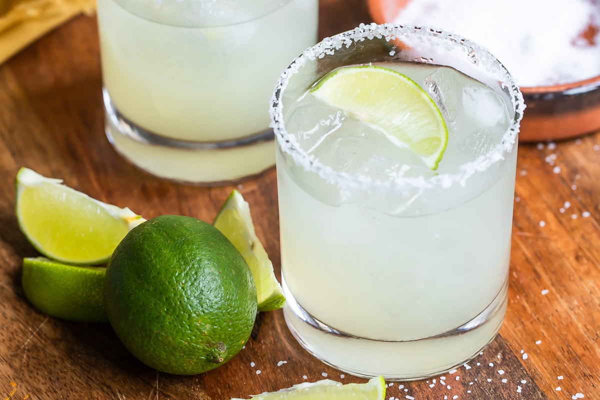 Two Margaritas on a wooden cutting board next to a lime.