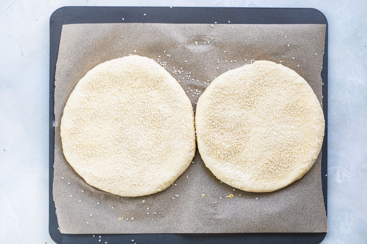 Muffaletta bread on a parchment lined baking sheet topped with sesame seeds.