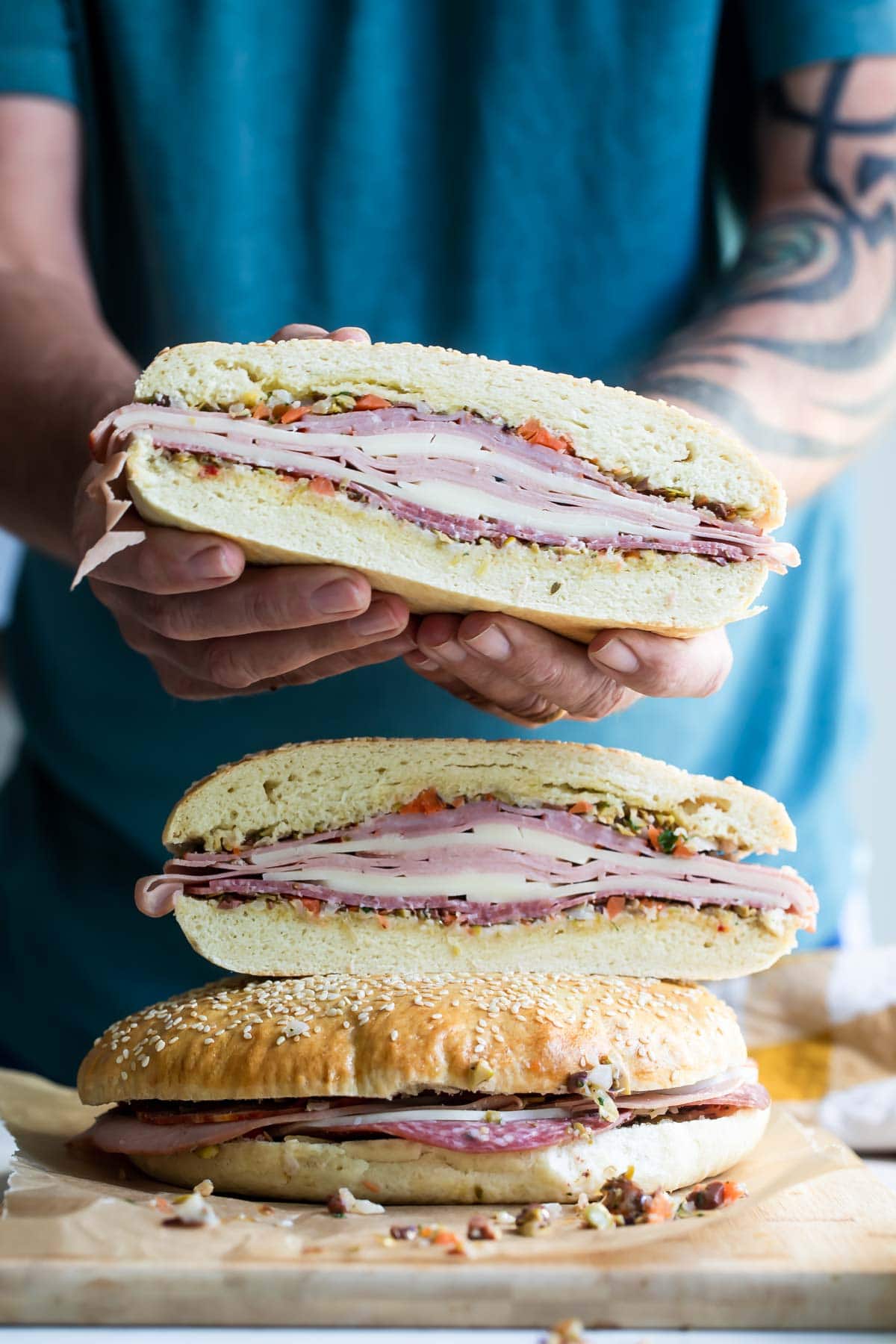 Someone holding a muffaletta sandwich half.