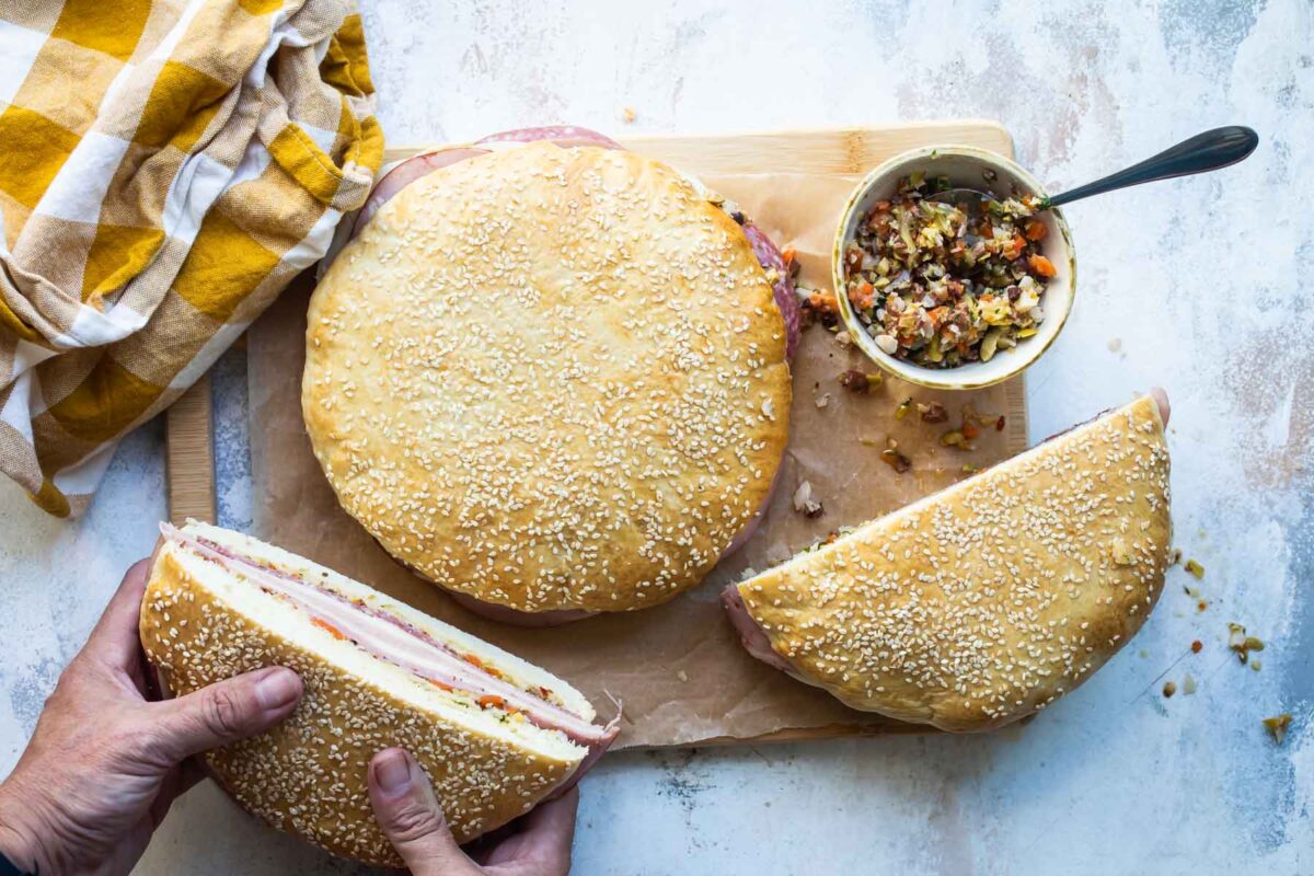 Someone holding a muffaletta sandwich half.