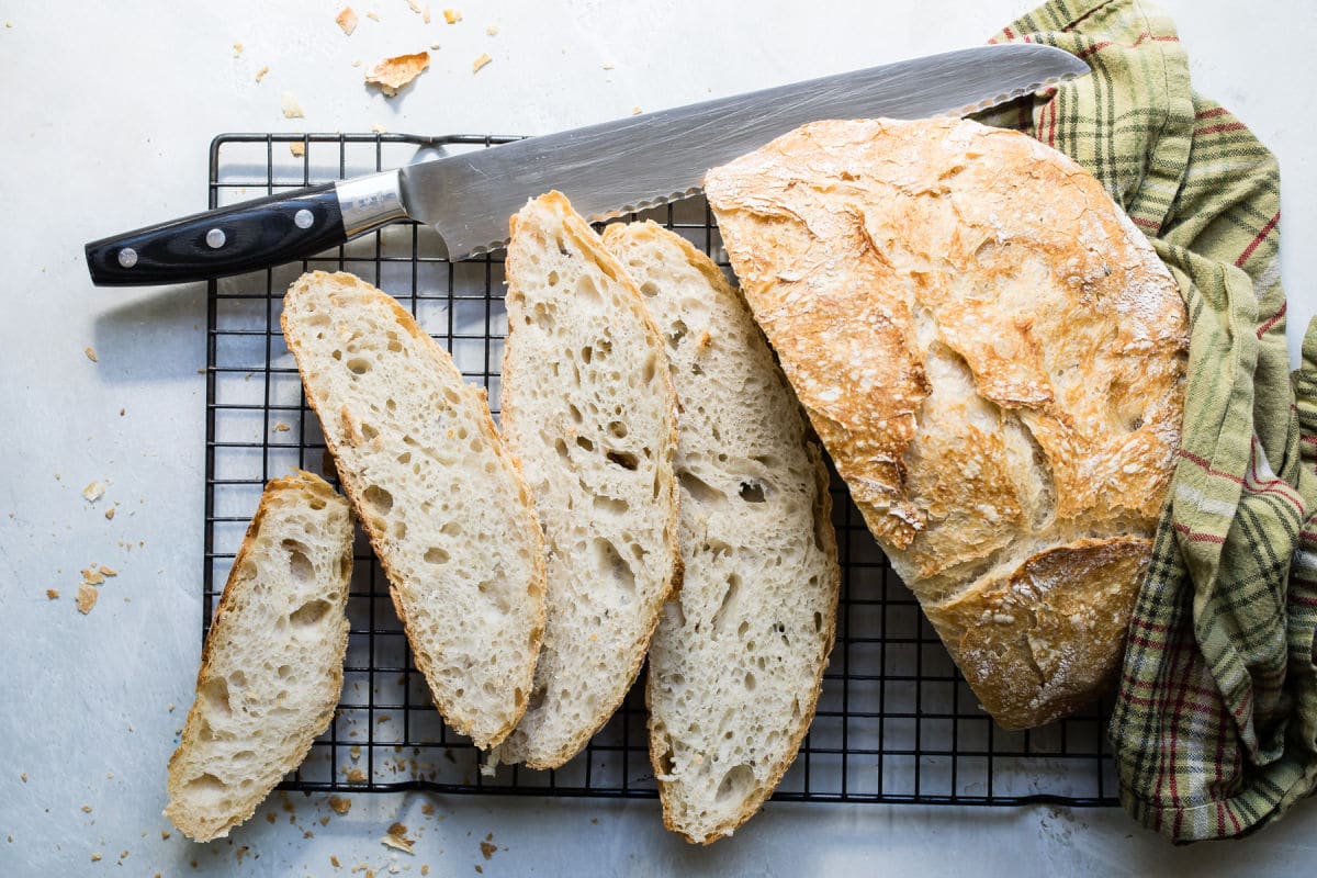 Sliced no knead bread on a cooling rack with a bread knife.