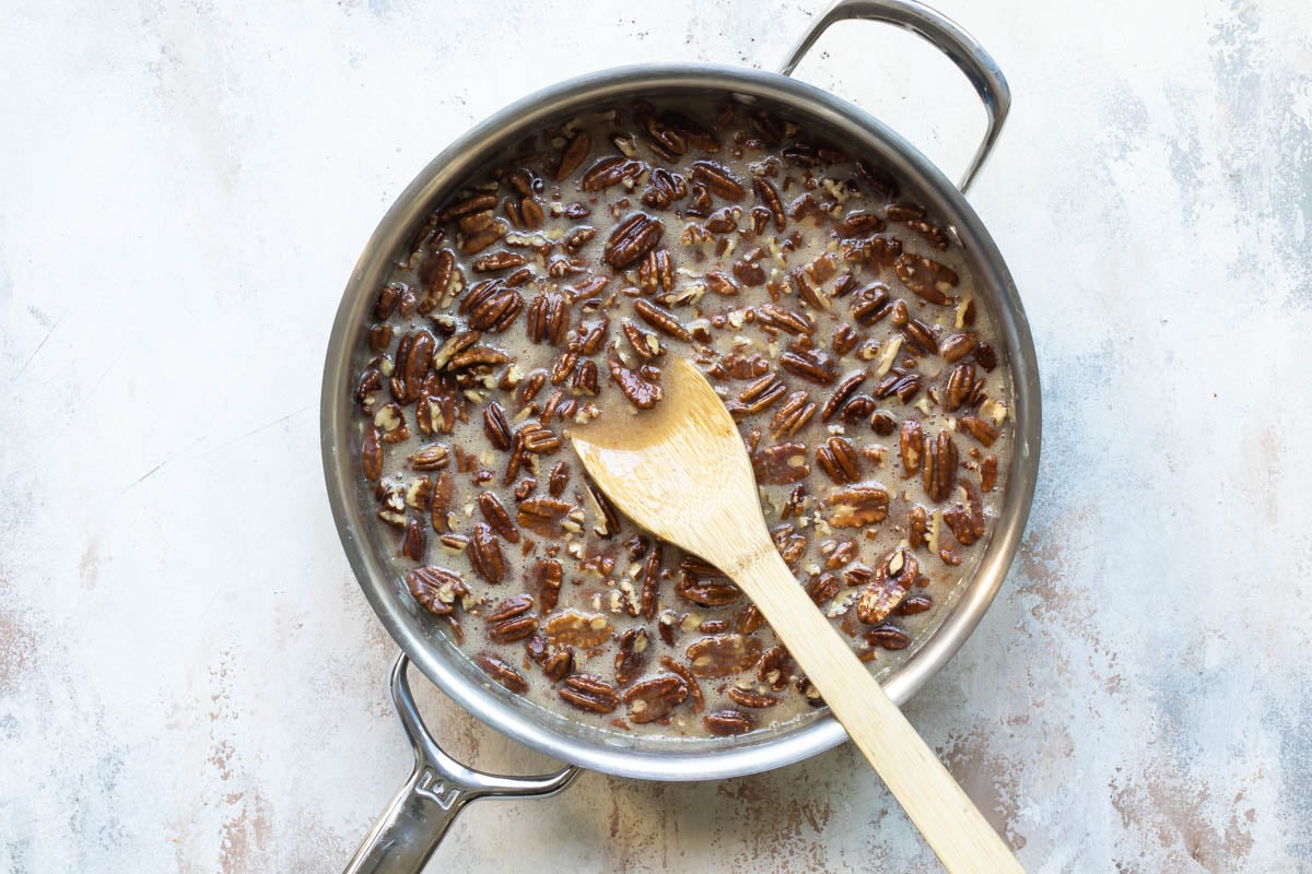 Pecan praline mixture in a silver pan with a wooden spoon resting in it.