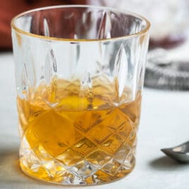 A Sazerac in a clear glass on a counter.