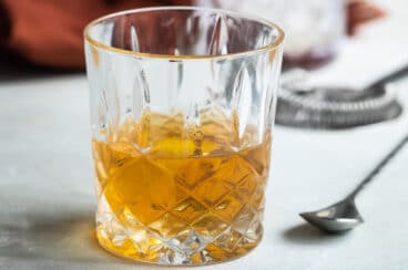 A Sazerac in a clear glass on a counter.