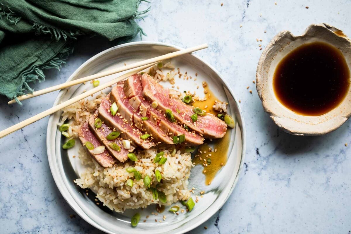 Ahi tuna on a small gray plate with rice and chopsticks.